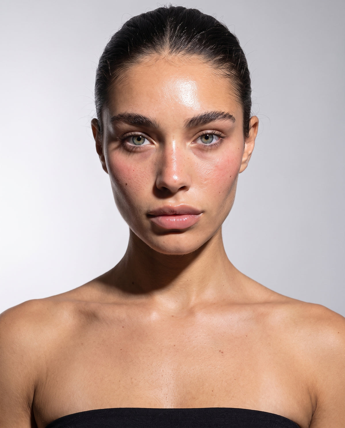 Close studio portrait of a woman with bare skin, hair scraped back, under a single hard key light
