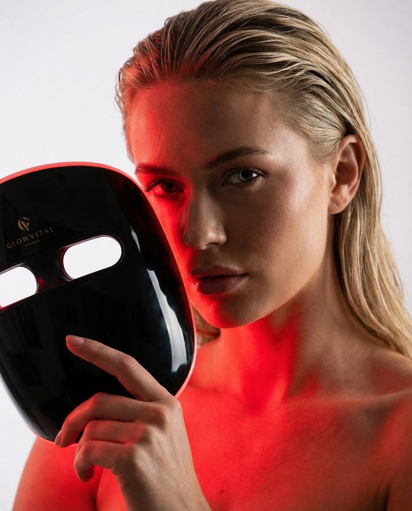 OmniGlow wireless LED light therapy mask. Black silicone face mask with red light mode active, on white background.